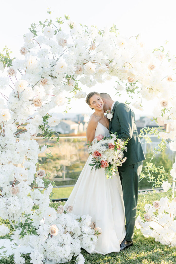 bride and groom kissing under floral arch at coastal maine ceremony
