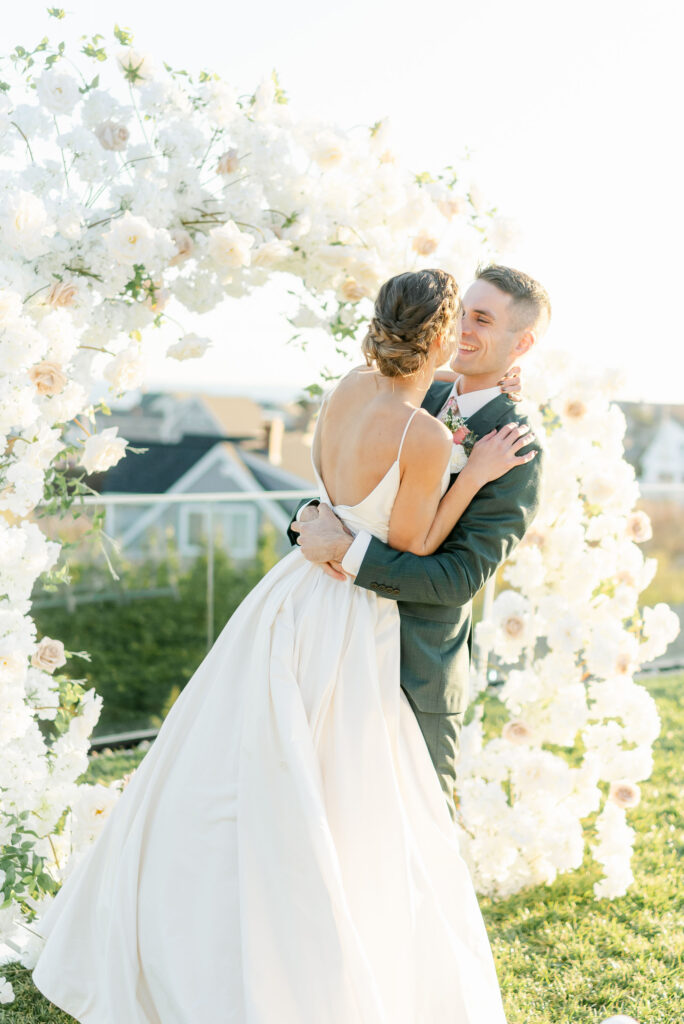 bride and groom kissing under floral arch at coastal maine ceremony