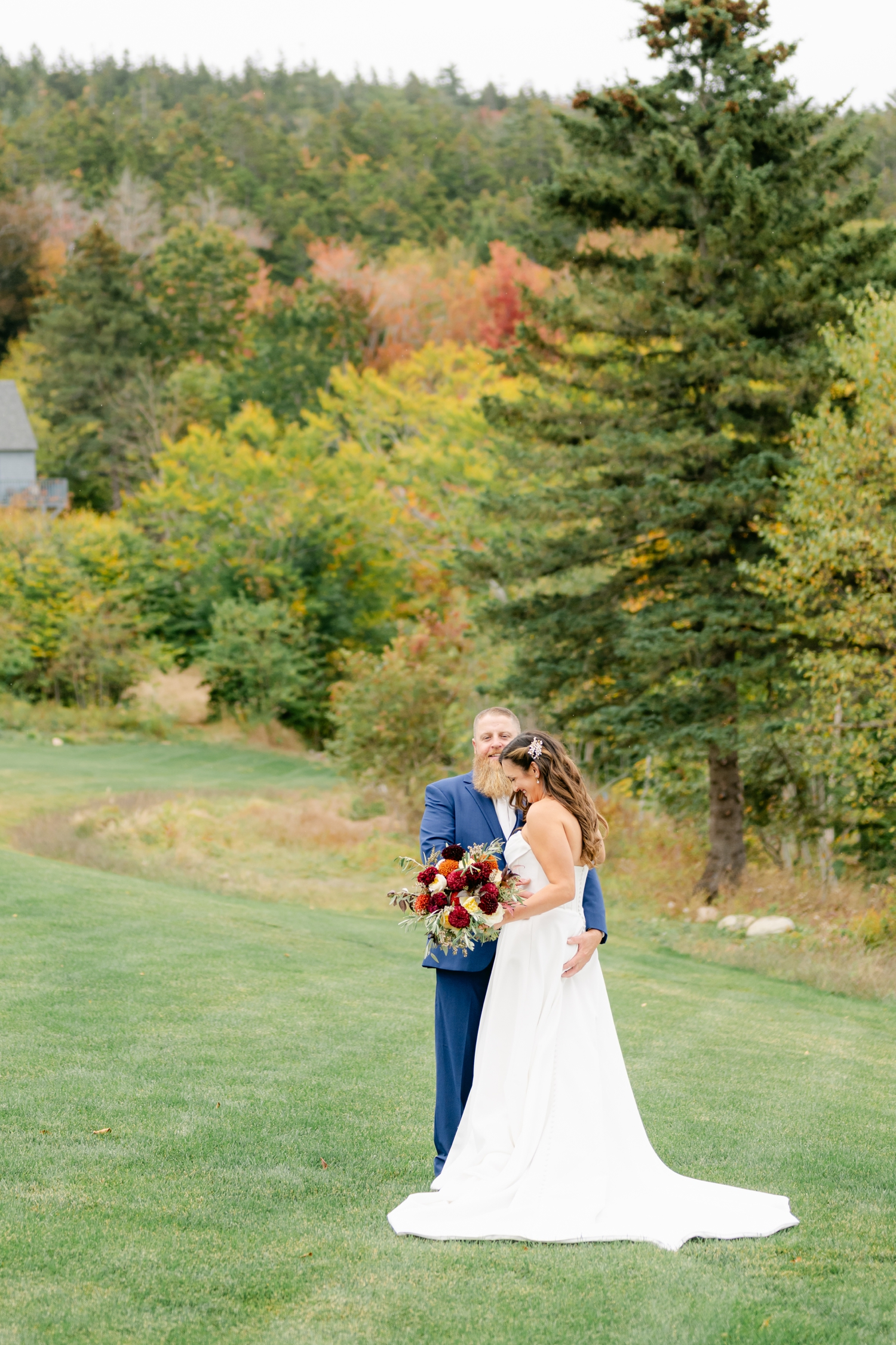 Bride and Groom standing outside the Asticou Inn during their autumn micro-wedding with soft foliage behind them.